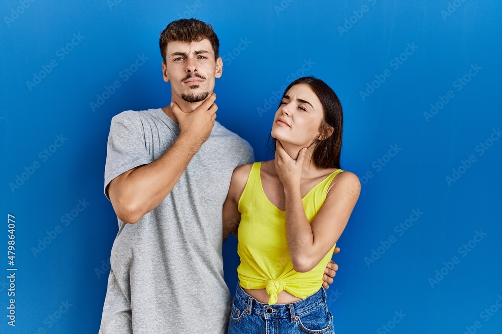 Obraz premium Young hispanic couple standing together over blue background touching painful neck, sore throat for flu, clod and infection