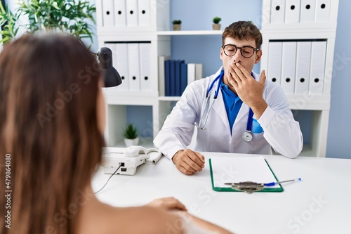 Fototapeta Naklejka Na Ścianę i Meble -  Young doctor with client at medical clinic bored yawning tired covering mouth with hand. restless and sleepiness.