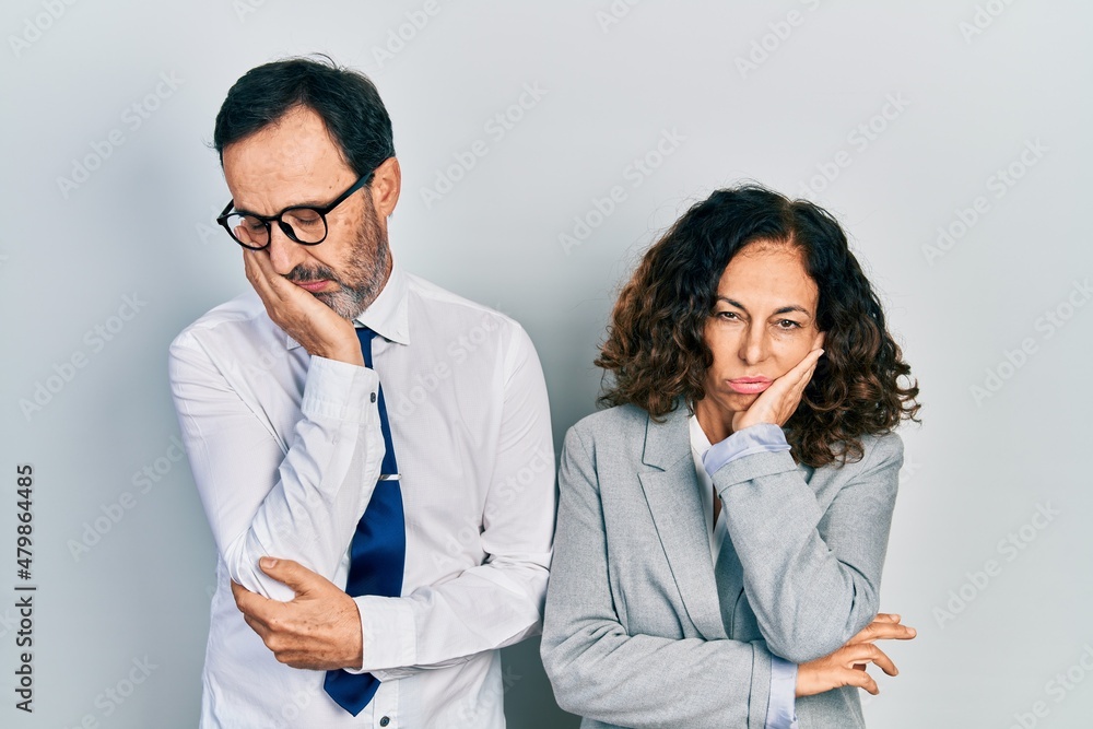 Middle age couple of hispanic woman and man wearing business office uniform thinking looking tired and bored with depression problems with crossed arms.