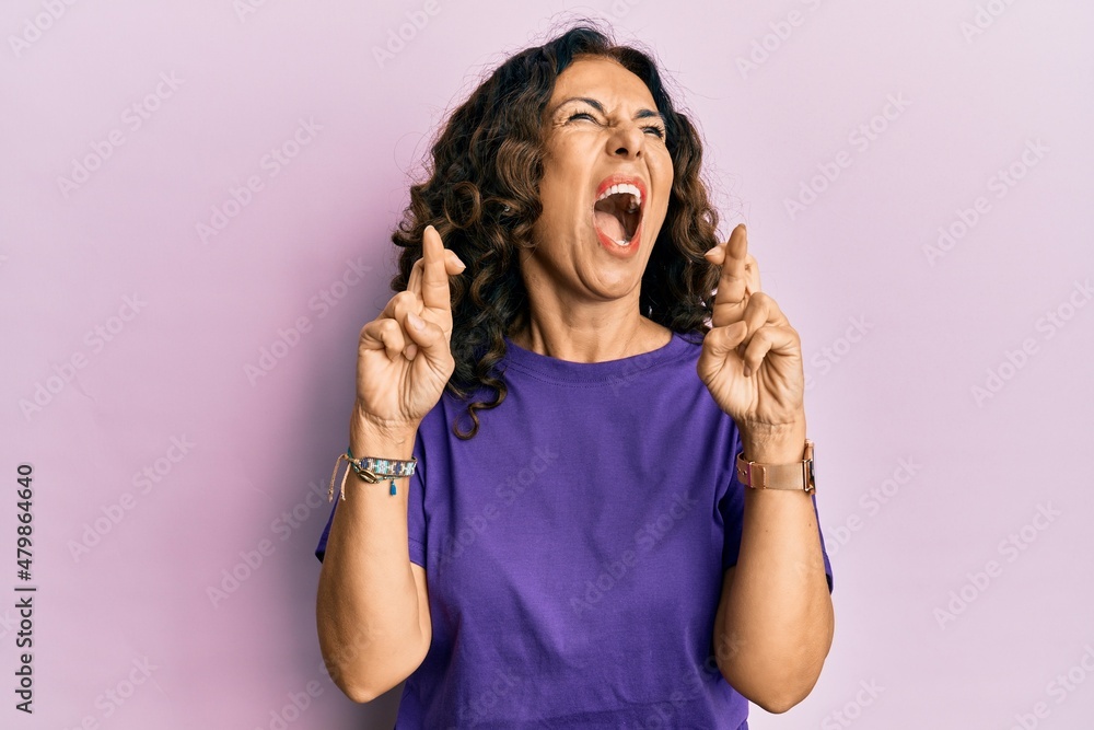 Middle age hispanic woman doing fingers crossed gesture angry and mad screaming frustrated and furious, shouting with anger looking up. Middle age hispanic woman doing fingers crossed gesture angry and mad screaming frustrated and furious, shouting with anger looking up.