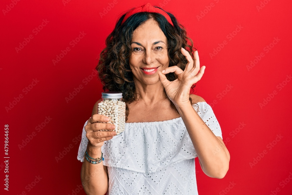 Middle age hispanic woman holding jar of beans doing ok sign with fingers, smiling friendly gesturing excellent symbol Middle age hispanic woman holding jar of beans doing ok sign with fingers, smiling friendly gesturing excellent symbol