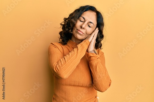 Middle age hispanic woman wearing casual clothes sleeping tired dreaming and posing with hands together while smiling with closed eyes.