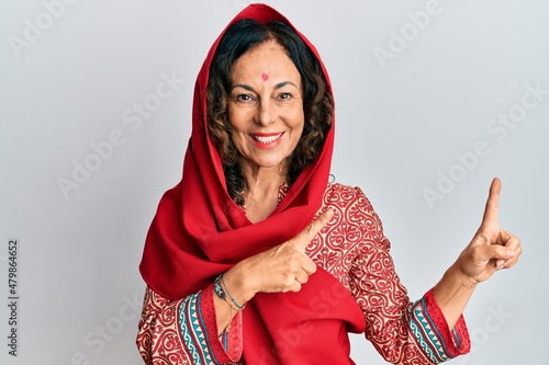 Middle age hispanic woman wearing tradition sherwani saree clothes smiling and looking at the camera pointing with two hands and fingers to the side.