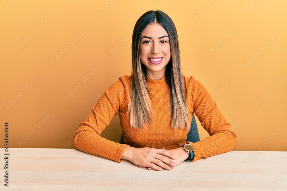 Young hispanic woman wearing casual clothes sitting on the table winking looking at the camera with sexy expression, cheerful and happy face. Young hispanic woman wearing casual clothes sitting on the table winking looking at the camera with sexy expression, cheerful and happy face.