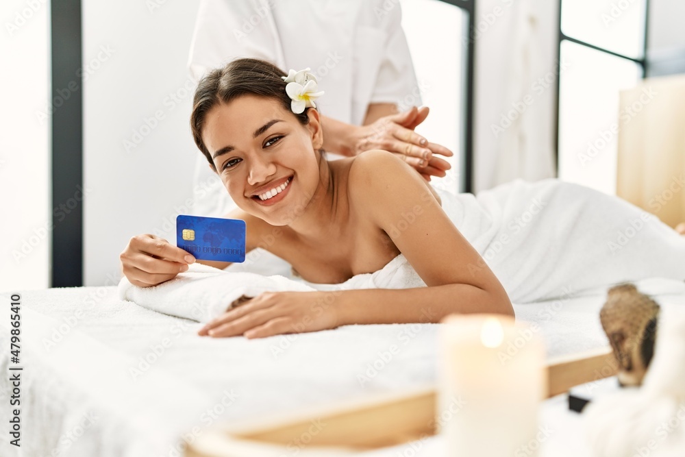 Young latin woman relaxed having back massage holding credit card at beauty center Young latin woman relaxed having back massage holding credit card at beauty center