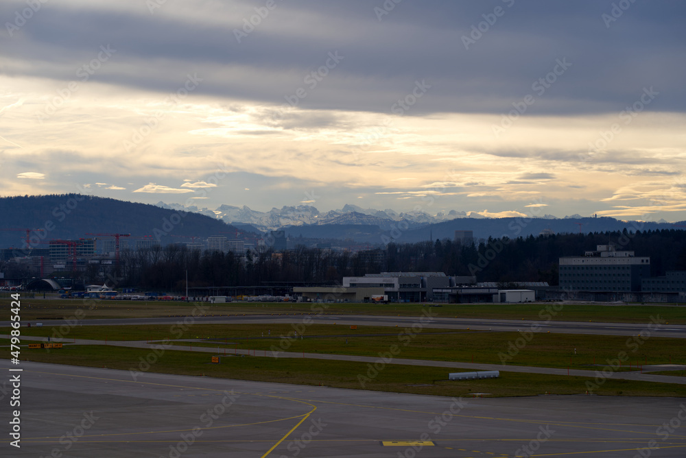 Zürich Airport with skyline of Zürich North and Swiss Alps in the background on a cloudy winter day. Photo taken January 2nd, 2022, Zurich, Switzerland.