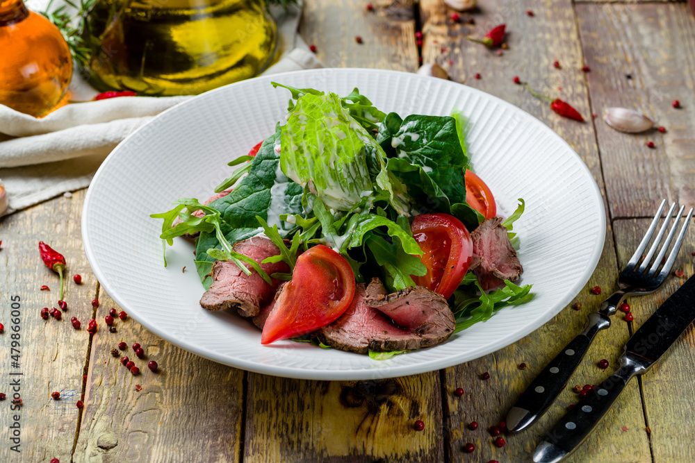 Salad with roast beef and vegetables on white plate on wooden table Salad with roast beef and vegetables on white plate on wooden table