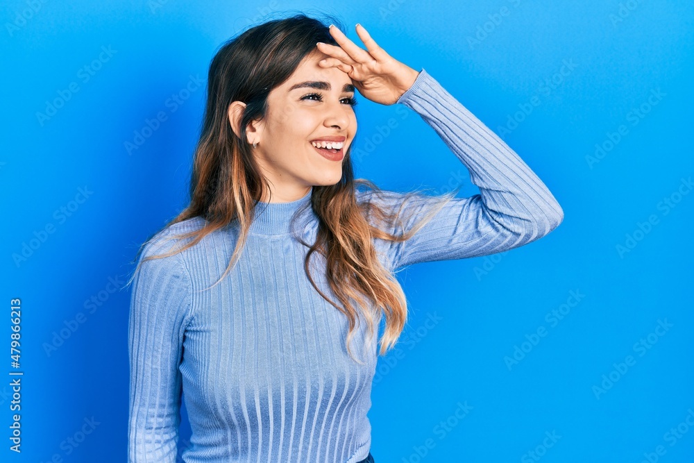 Young hispanic girl wearing casual clothes very happy and smiling looking far away with hand over head. searching concept.