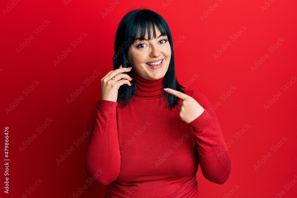 Young hispanic woman having conversation talking on the smartphone smiling happy pointing with hand and finger Young hispanic woman having conversation talking on the smartphone smiling happy pointing with hand and finger