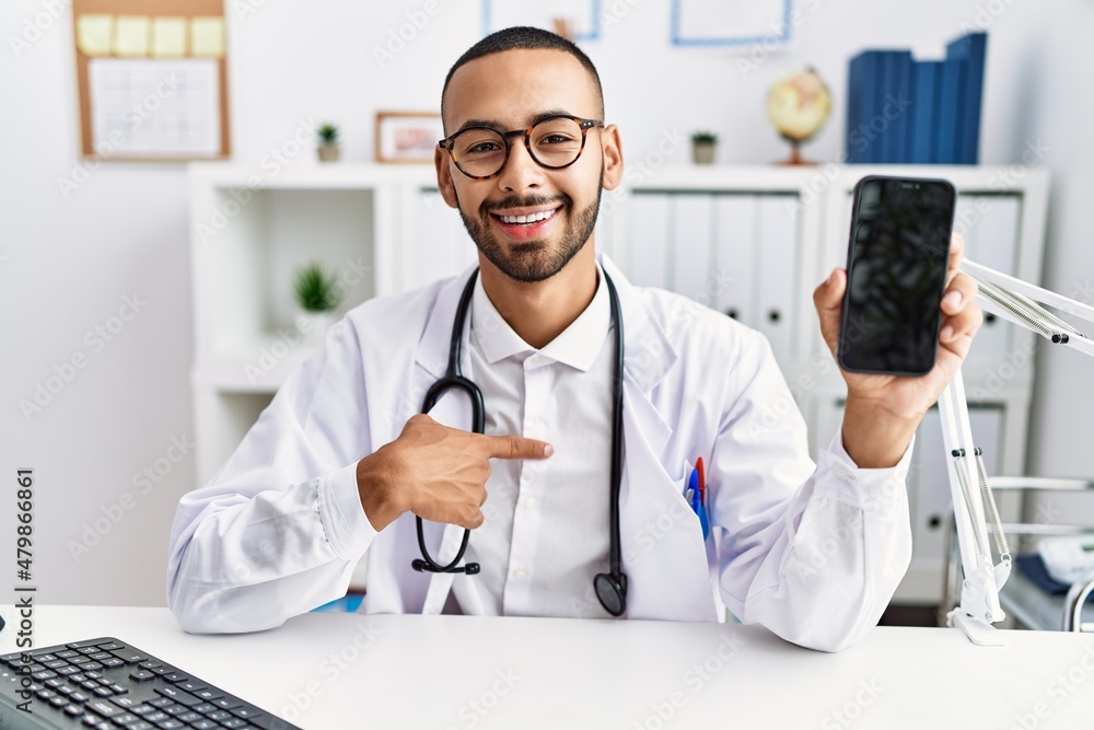 African american doctor man holding smartphone showing blank screen at the clinic pointing finger to one self smiling happy and proud African american doctor man holding smartphone showing blank screen at the clinic pointing finger to one self smiling happy and proud