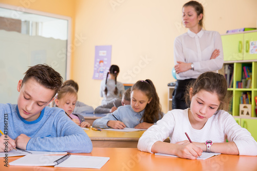 Group of school kids with pens and notebooks studying in classroom with teacher