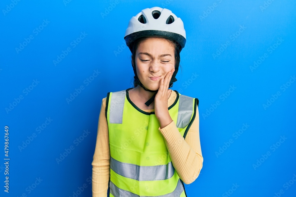 Beautiful brunette little girl wearing bike helmet and reflective vest touching mouth with hand with painful expression because of toothache or dental illness on teeth. dentist Beautiful brunette little girl wearing bike helmet and reflective vest touching mouth with hand with painful expression because of toothache or dental illness on teeth. dentist