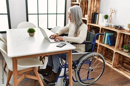 Middle age grey-haired woman uisng laptop sitting on wheelchair at home © Krakenimages.com