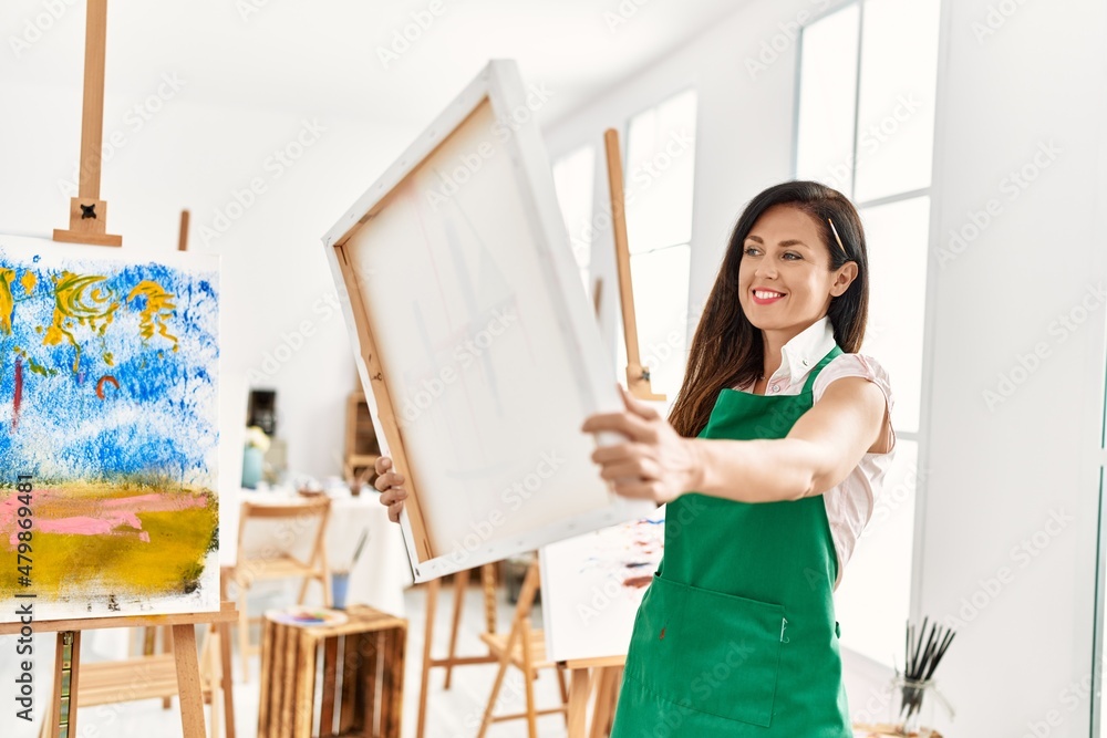 Middle age hispanic woman smiling confident holding canvas draw at art studio Middle age hispanic woman smiling confident holding canvas draw at art studio