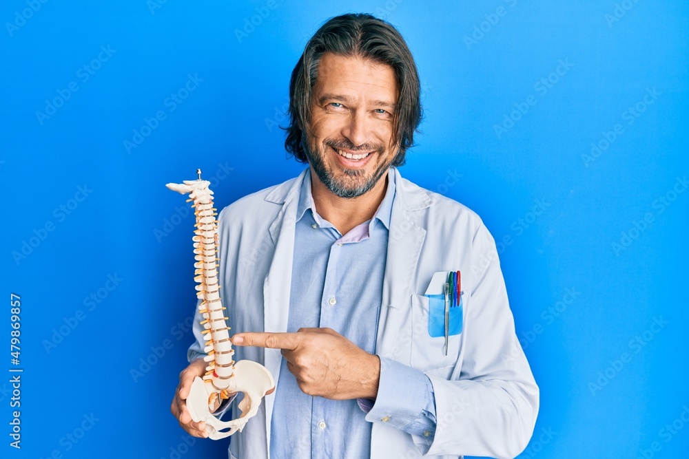 Fototapeta premium Middle age handsome traumatologist man holding anatomical model of spinal column smiling with a happy and cool smile on face. showing teeth.