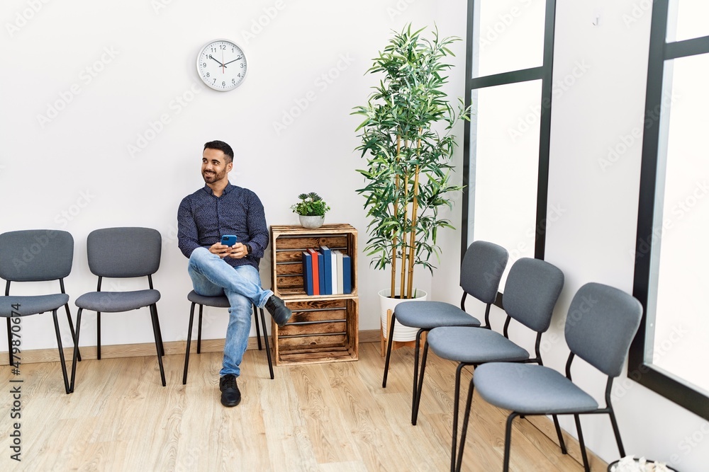 Young hispanic man using smartphone sitting on chair at waiting room Young hispanic man using smartphone sitting on chair at waiting room