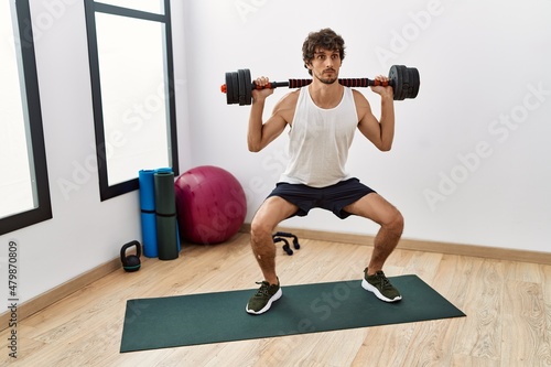 Young hispanic man training using dumbbells at sport center