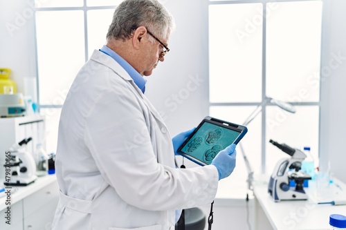 Middle age grey-haired man wearing scientist uniform looking embryology image touchpad at laboratory photo