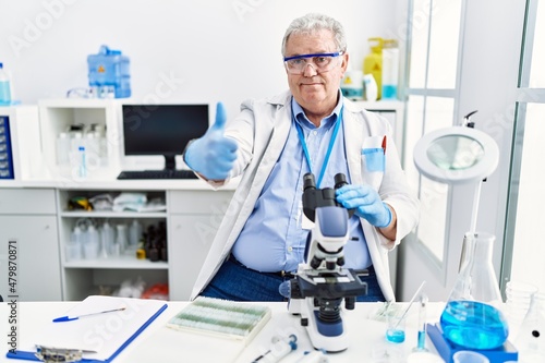 Senior caucasian man working at scientist laboratory approving doing positive gesture with hand  thumbs up smiling and happy for success. winner gesture.