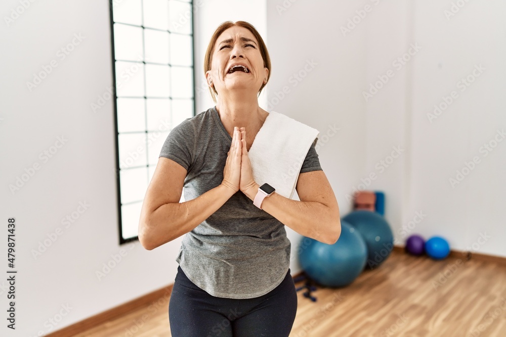 Middle age woman wearing sporty look training at the gym room begging and praying with hands together with hope expression on face very emotional and worried. begging.