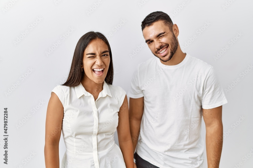 Young interracial couple standing together in love over isolated background winking looking at the camera with sexy expression, cheerful and happy face. Young interracial couple standing together in love over isolated background winking looking at the camera with sexy expression, cheerful and happy face.