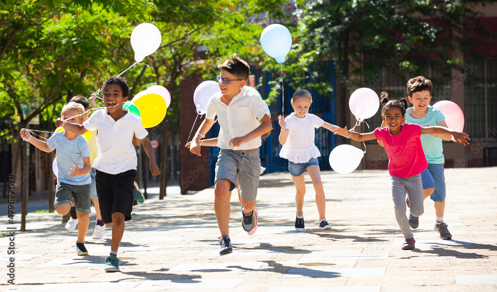 Obraz premium Group of happy kids with balloons running in race in the street and laughing outdoors