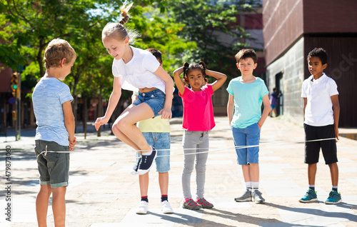 Happy smiling little friends playing with chinese jumping rope at playground. High quality photo