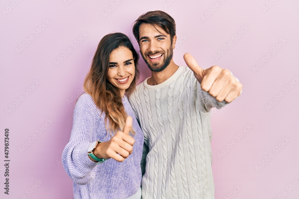 Fototapeta premium Young hispanic couple wearing casual clothes approving doing positive gesture with hand, thumbs up smiling and happy for success. winner gesture.