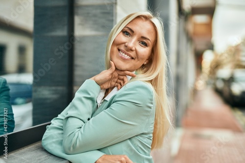 Young blonde businesswoman smiling happy standing at the city