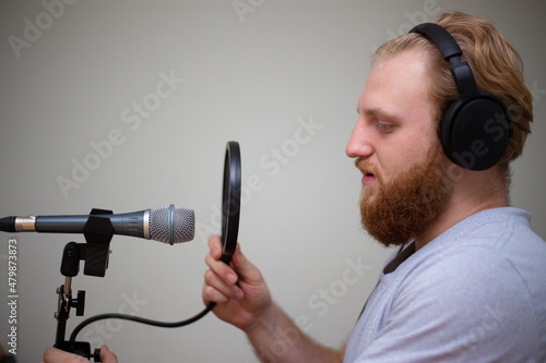 A young guy with a beard sings into a studio microphone with a pop filter