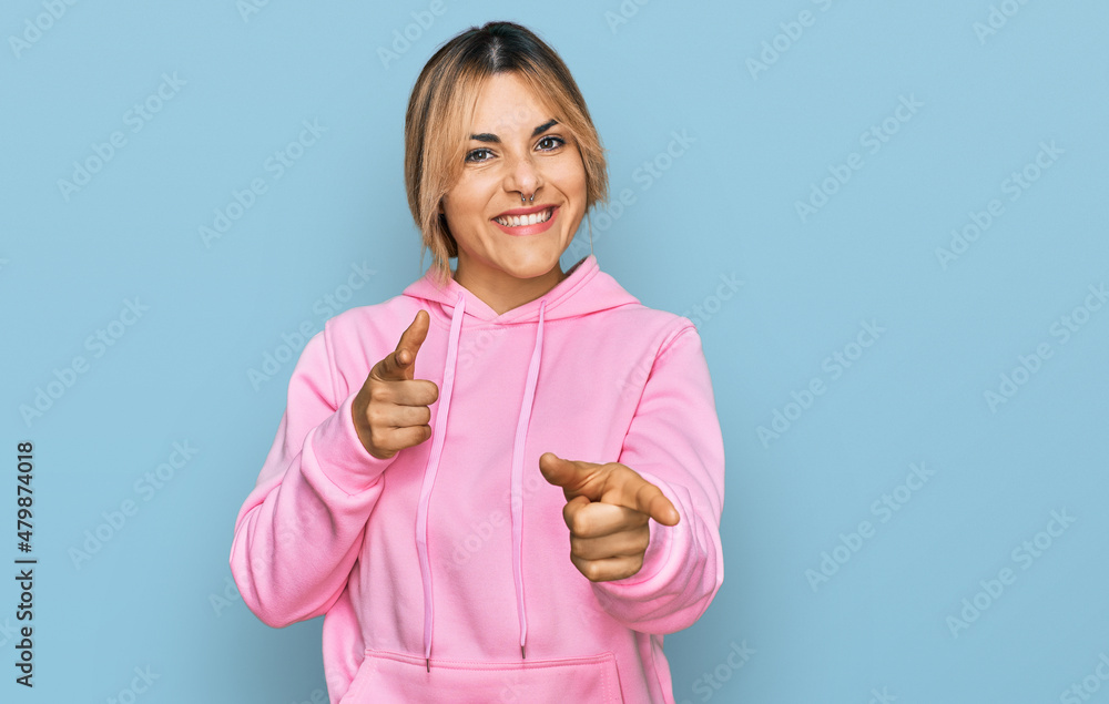 Young caucasian woman wearing casual sweatshirt pointing fingers to camera with happy and funny face. good energy and vibes. Young caucasian woman wearing casual sweatshirt pointing fingers to camera with happy and funny face. good energy and vibes.
