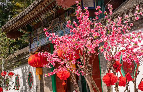 artificial peach blossoms on a branch and decorations in Vintage Historical Chinese House Structure for chinese new year,calligraphy Translation:good bless for new