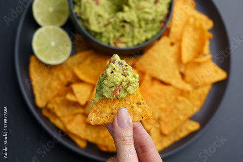 Top view of woman hand holding tortilla chips or nachos with tasty guacamole dip