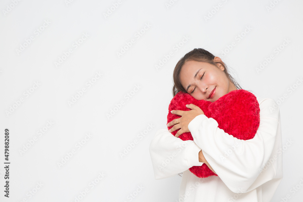 Beautiful Asian woman wearing white sweater closing her eyes and hugging red heart shape pillow on white background and copy space for Valentine Day concept. Beautiful Asian woman wearing white sweater closing her eyes and hugging red heart shape pillow on white background and copy space for Valentine Day concept.