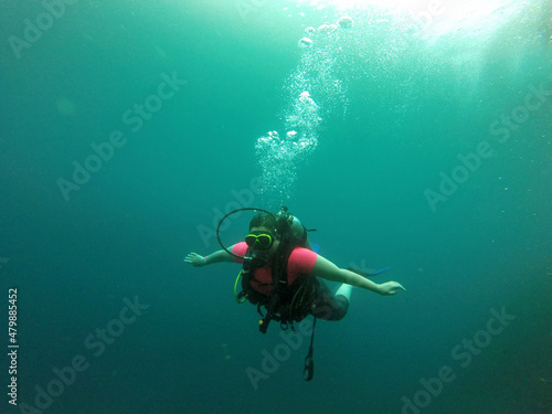 Wallpaper Mural Young woman practices the sport scuba diving with oxygen tank equipment, visor, fins, relaxes and enjoys the bottom of the crystal clear water next to large branches and trunks
 Torontodigital.ca