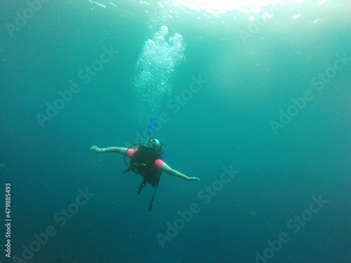 Young woman practices the sport scuba diving with oxygen tank equipment, visor, fins, relaxes and enjoys the bottom of the crystal clear water next to large branches and trunks 