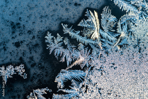 Frost on glass creeps across the frame.  Crystals and foggy glass, winter cold concept, macro view.  Close up of ice crystals forming on window.