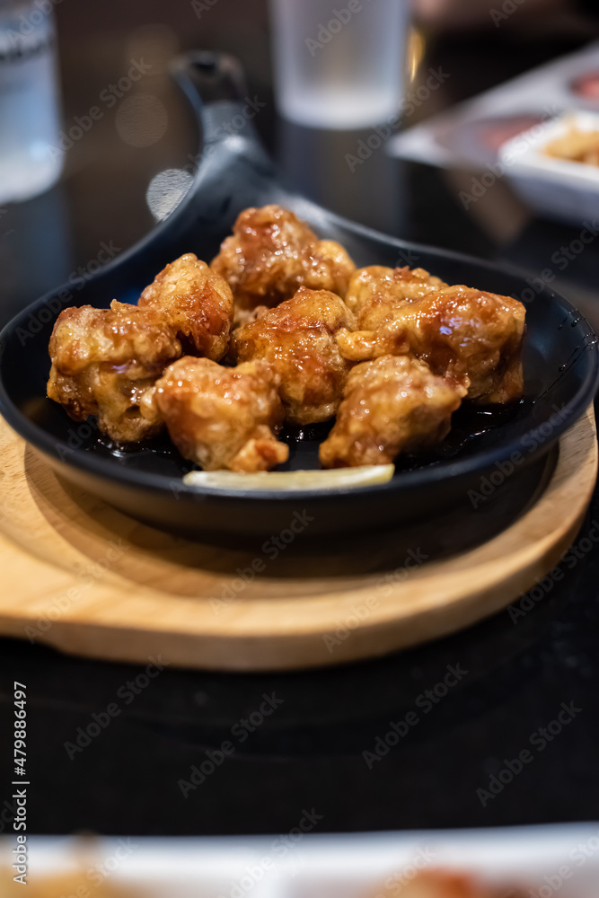Fried chicken with soy sauce served on the black hot plate with kimchi on table. Traditional Korean Crispy Chicken in a modern Korean restaurant.