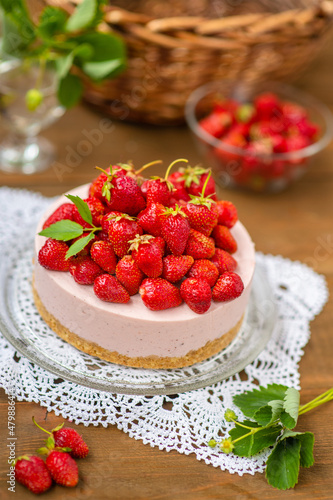 Strawberry cheesecake with a decor of a large number of strawberries and violet flowers lying on a lace napkin on a wooden background