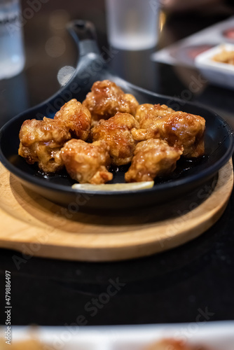 Fried chicken with soy sauce served on the black hot plate with kimchi on table. Traditional Korean Crispy Chicken in a modern Korean restaurant.
