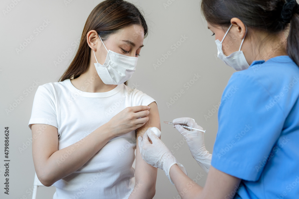 Asian woman wearing a medical mask receives coronavirus vaccine from a doctor. People are vaccinated against COVID-19 to prevent infection with the virus and stop its spread.
