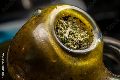 Macro view of a dirty green glass pipe, with finely ground marijuana in the bowl.  Bubbler pipe that needs to be cleaned, close up of medical marijuana ready for use.