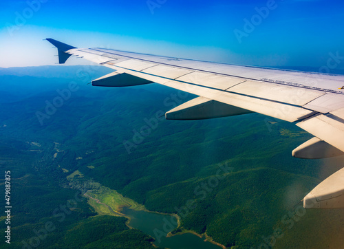 View of airplane wing, blue skies and green land during landing. Airplane window view.