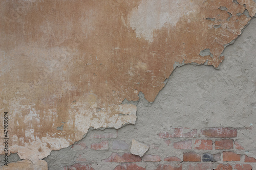Old stone wall covered with cement. Half of cement on this wall is crumbled. There are bricks under the cement.	