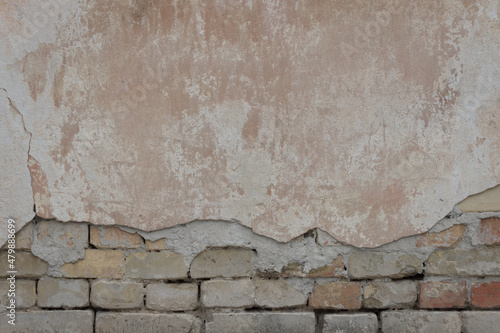 Old stone wall covered with cement. Half of cement on this wall is crumbled. There are bricks under the cement.	