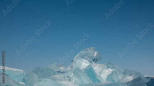 A bizarre block of turquoise ice hummocks against a clear blue sky. Sun glare on the edges. Close-up. Copy Space