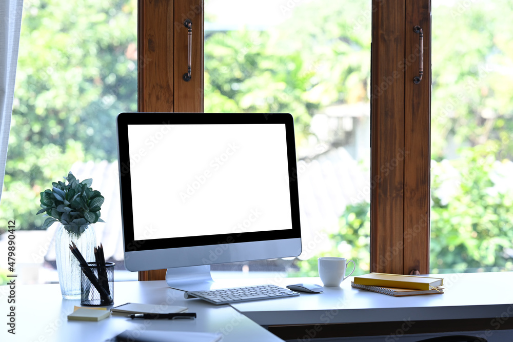 Fototapeta premium Mockup computer with blank screen and office supplies on white table at creative workplace.