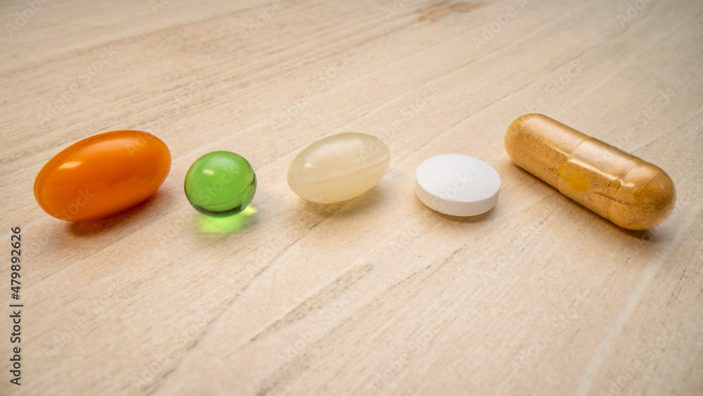 vitamins and supplements, row of pills, capsules and tablets on a wood background, macro shot, healthcare, self care and wellbeing concept