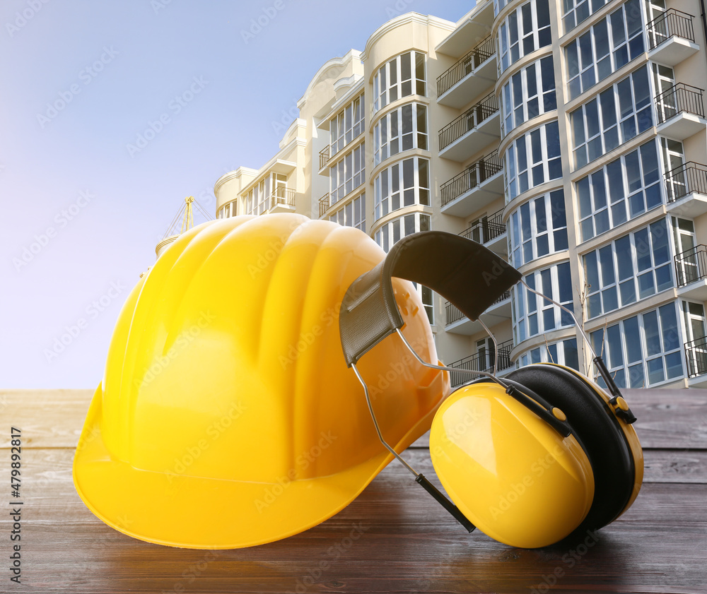 Safety hardhat and ear muffs on wooden table at construction site Safety hardhat and ear muffs on wooden table at construction site
