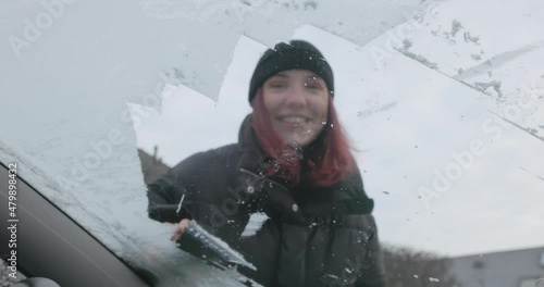 Winter Driving - Scraping ice off the frozen windshield of a car  - slow motion - windscreen in focus - ProRes

A hand-held shot, showing a young woman who is clearing the frozen windshield of her car